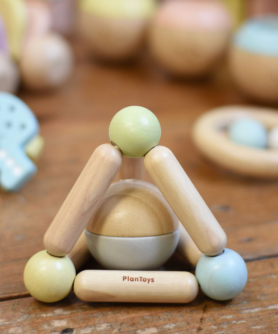 A PlanToys Pastel Triangle Clutching Toy placed on a wooden floor surrounded by other toys from the PlanToys pastel baby collection. 