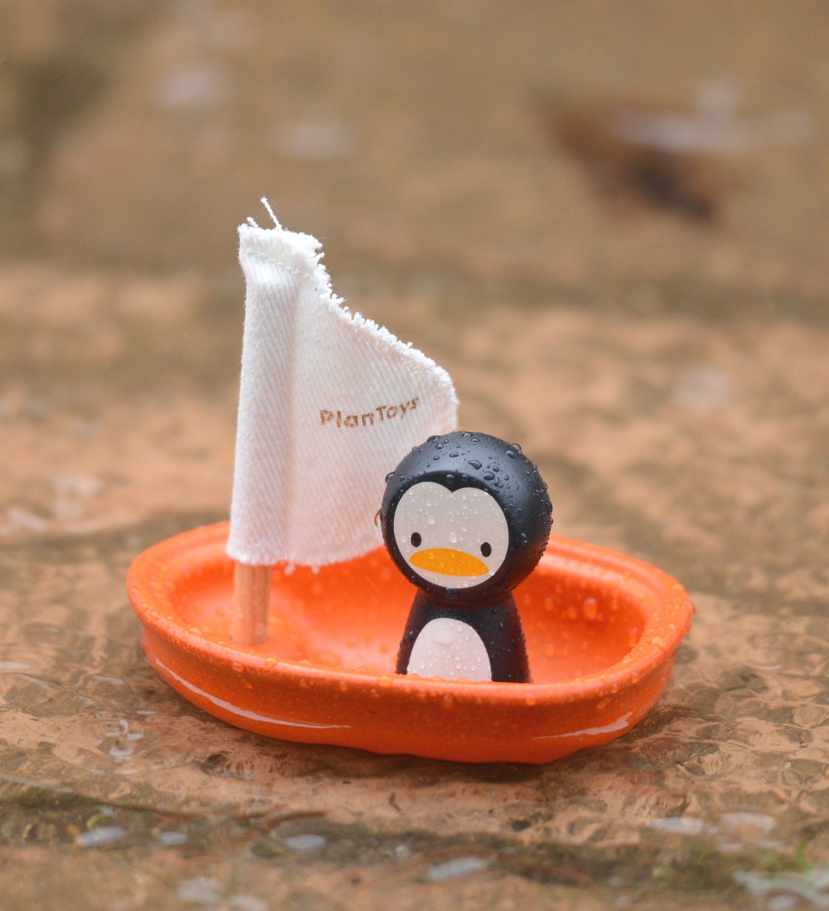 The PlanToys Penguin Sailing Boat placed on wet stone surface. 