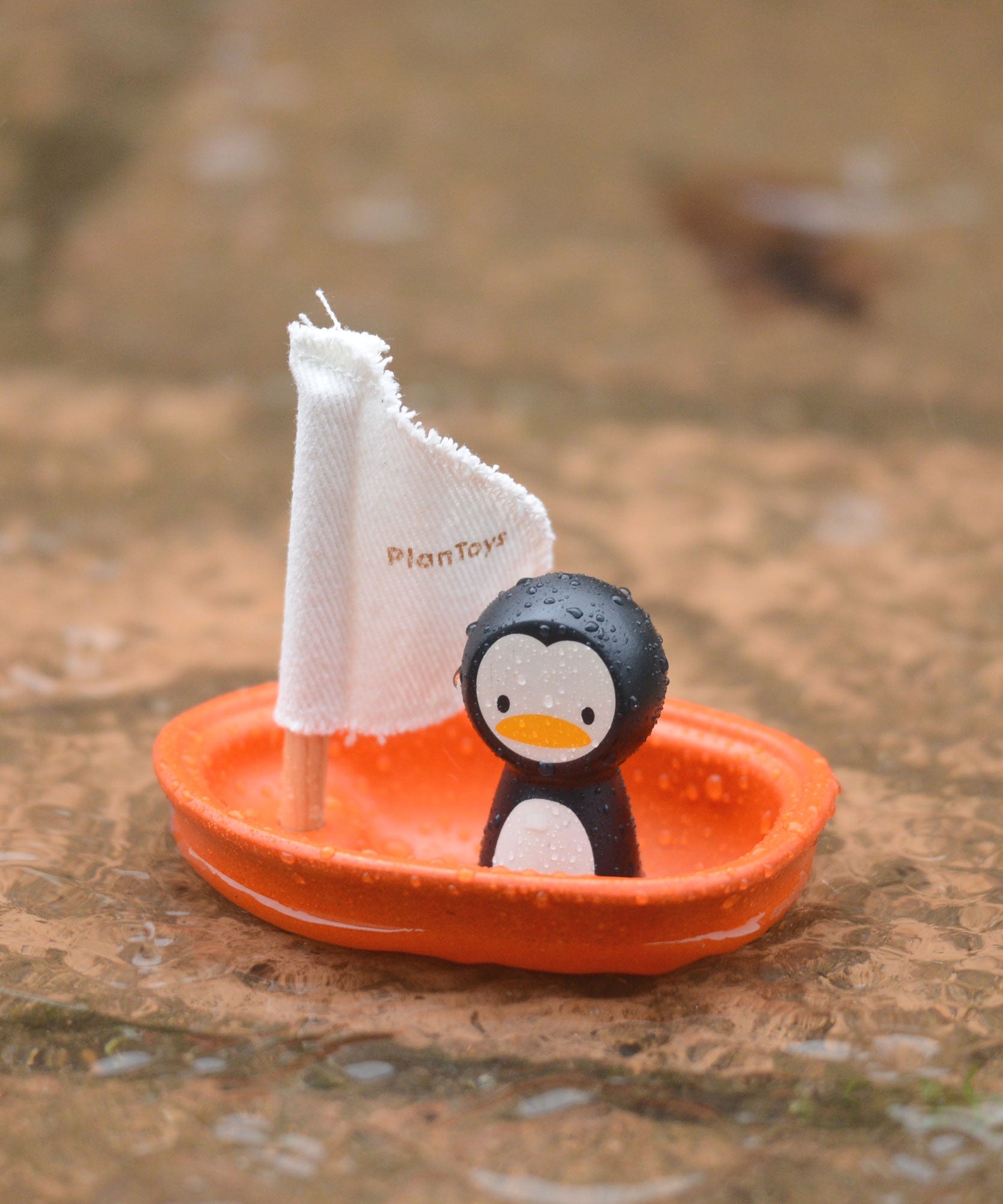 The PlanToys Penguin Sailing Boat placed on wet stone surface. 