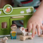 A child's hand playing with the PlanToys wooden pet shop and dog.