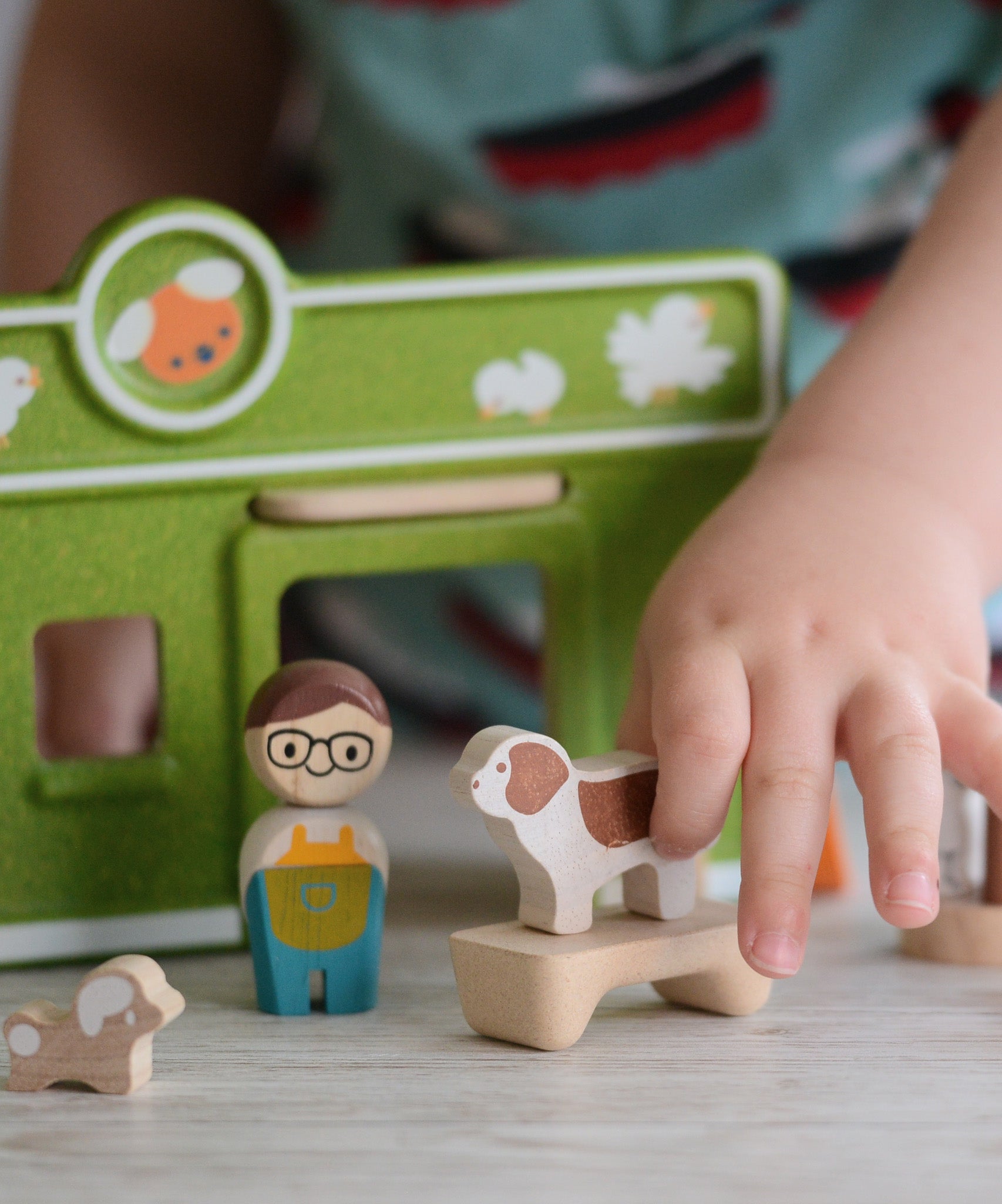 A child's hand playing with the PlanToys wooden pet shop and dog.