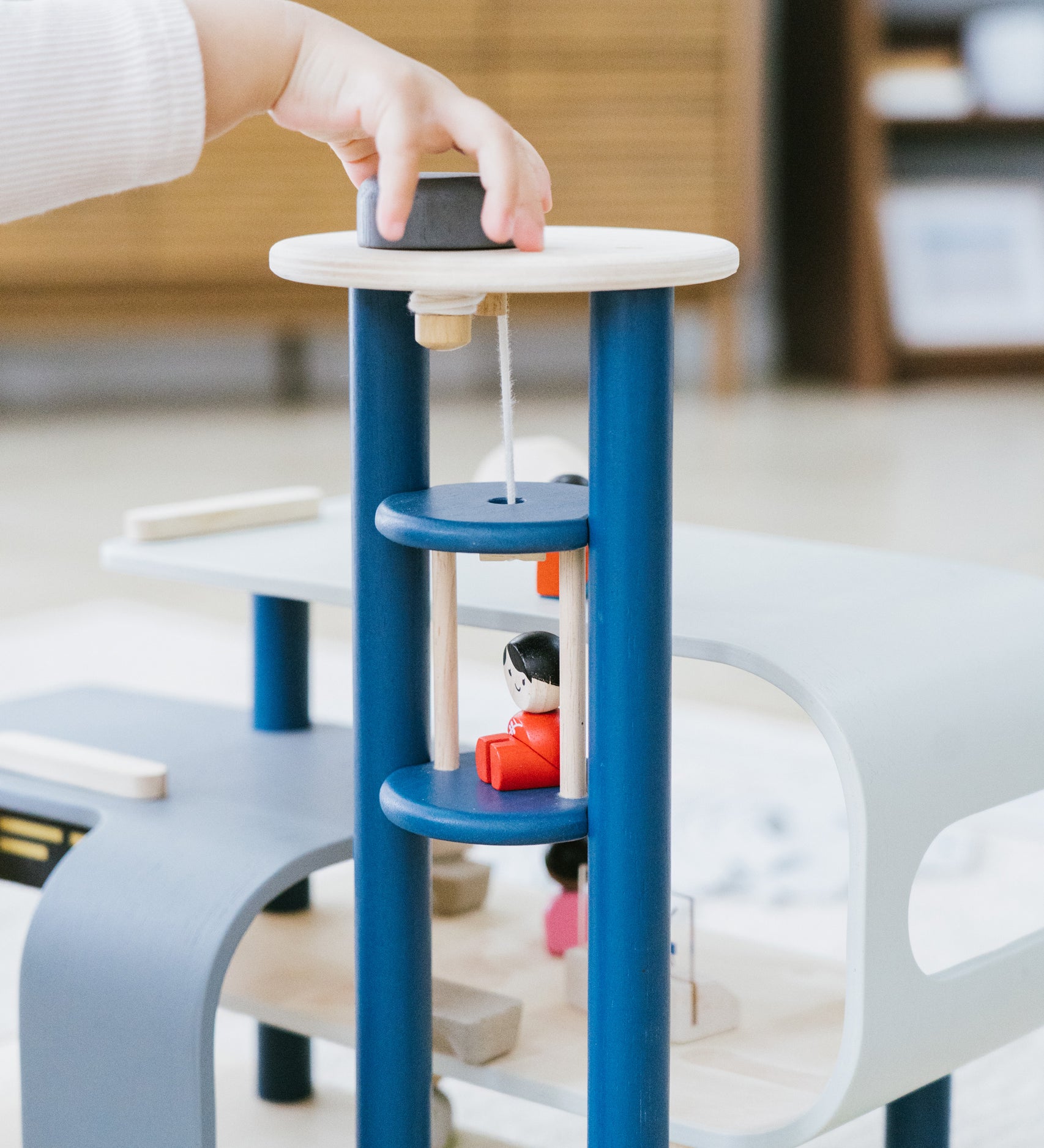 A close up of a child's hand playing with the PlanToys PlanWorld Central Station Wooden toy. They are operating the lift part.
