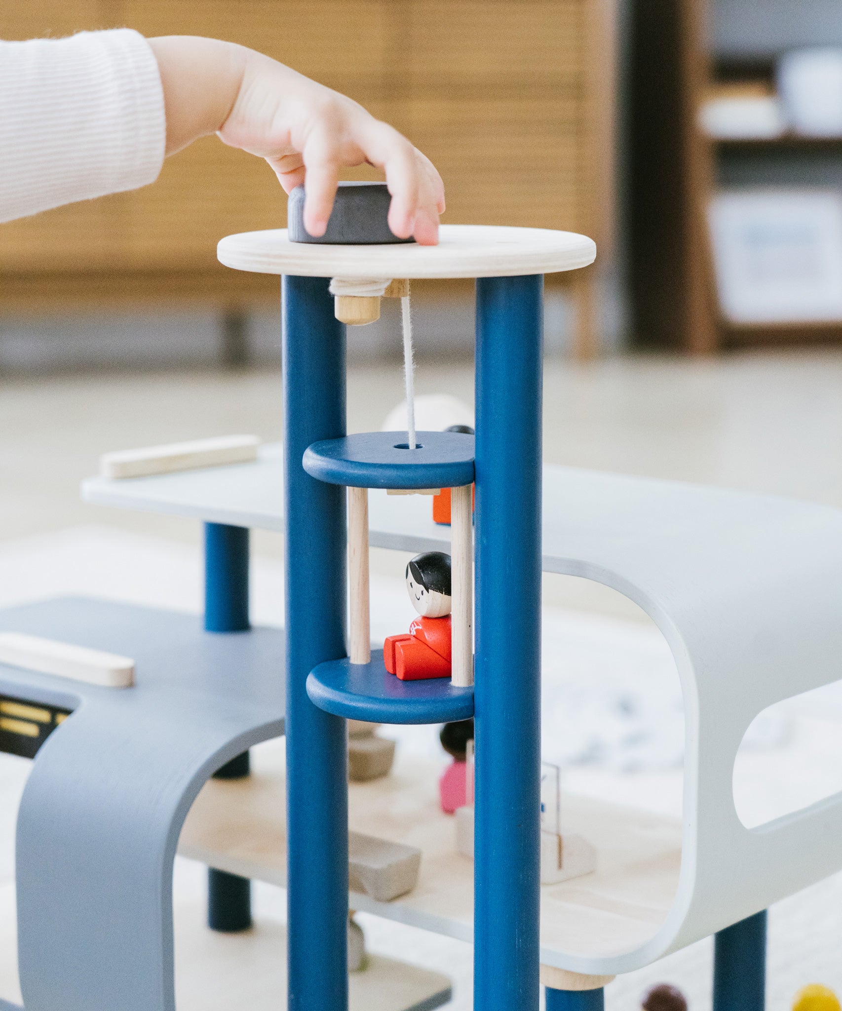 A close up of a child's hand playing with the PlanToys PlanWorld Central Station Wooden toy. They are operating the lift part.
