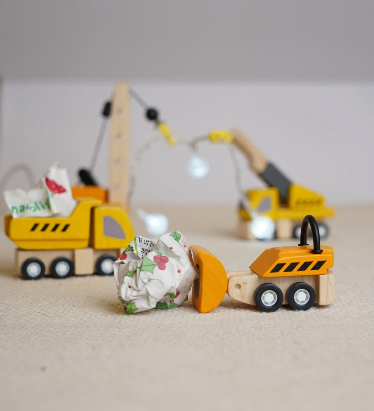 The PlanToys PlanWorld Construction Vehicles Set placed on a light coloured rug, the dozer is pushing a rolled up ball of paper along and the dumper has a piece in it's trainer. 