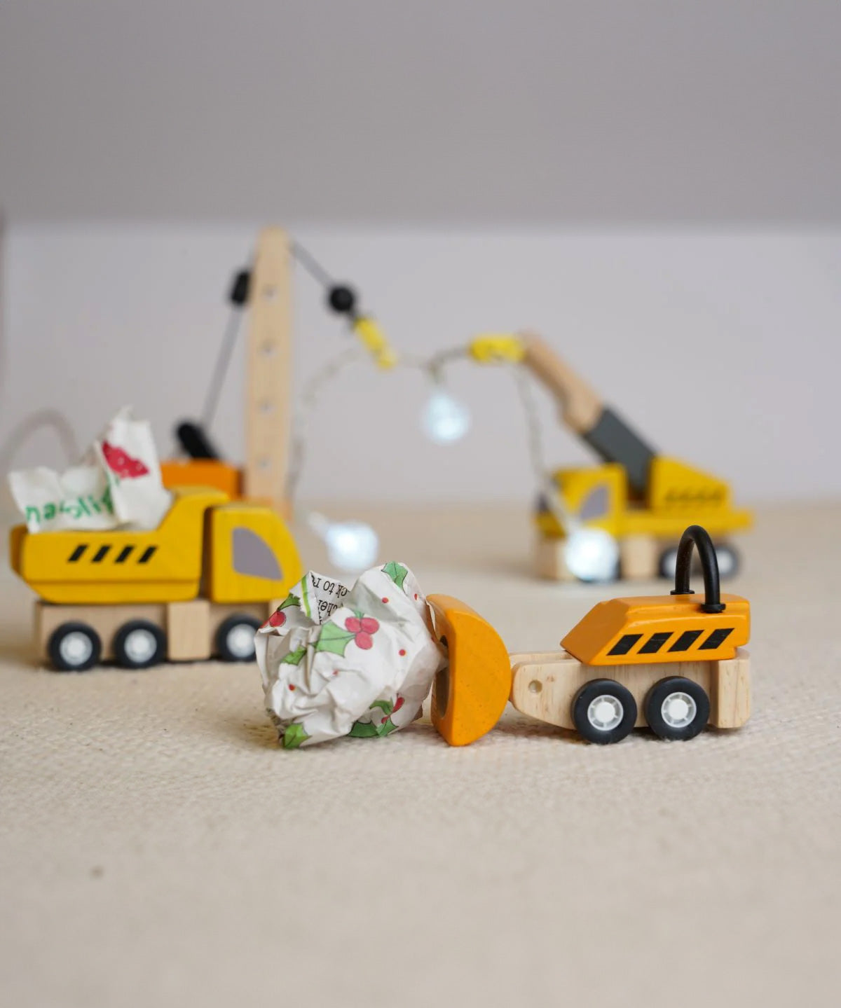 The PlanToys PlanWorld Construction Vehicles Set placed on a light coloured rug, the dozer is pushing a rolled up ball of paper along and the dumper has a piece in it's trainer. 