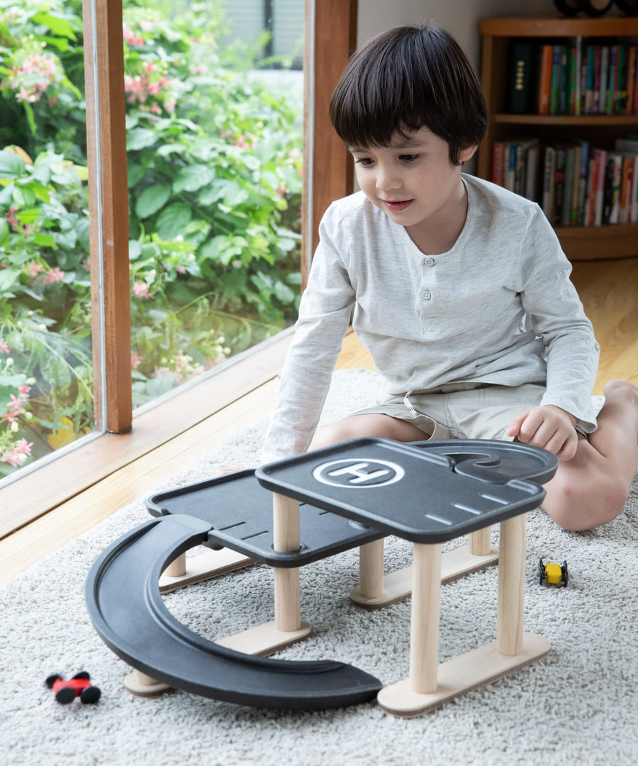 A child sitting on a rug playing with the PlanToys PlanWorld Race N Play Parking Garage.