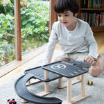 A child sitting on a rug playing with the PlanToys PlanWorld Race N Play Parking Garage.