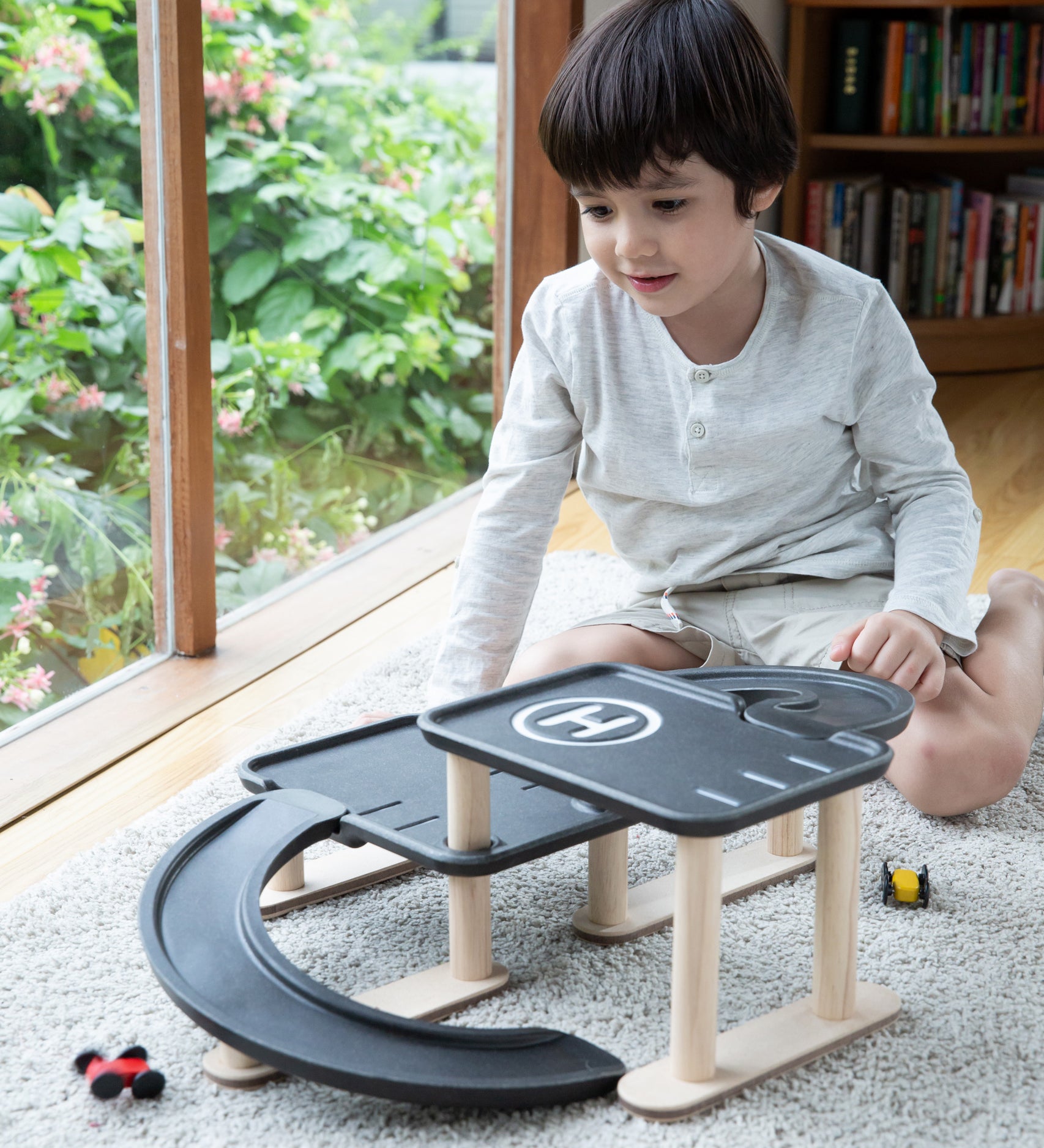 A child sitting on a rug playing with the PlanToys PlanWorld Race N Play Parking Garage.