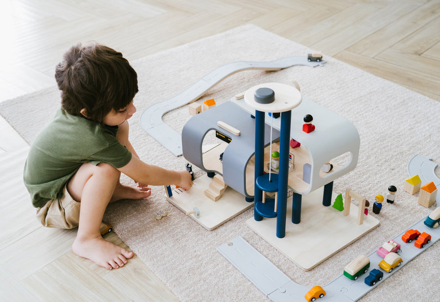 A child crouching down playing with the PlanToys PlanWorld Central Station Wooden toy on a rug. 
