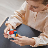 Close up of young boy holding the PlanToys rectangular stacking blocks puzzle toy. The boy is sitting at the PlanToys desk. 