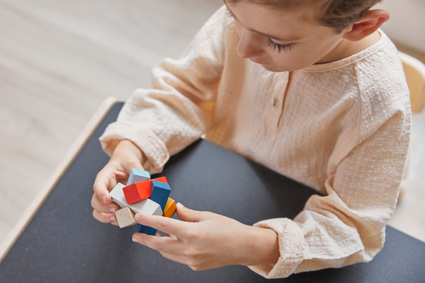 Close up of young boy holding the PlanToys rectangular stacking blocks puzzle toy. The boy is sitting at the PlanToys desk. 