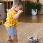 Child walking backwards on a beige carpet pulling the PlanToys wooden musical xylophone bear toy