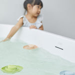 Close up of 3 PlanToys natural rubber bath toys floating in some water in front of a young girl