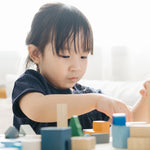 Close up of a young girl playing with the PlanToys plastic-free urban city blocks on a white table