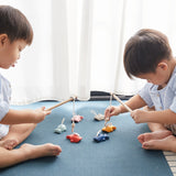 Two children sat on a blue carpet playing with the PlanToys fish hooking game