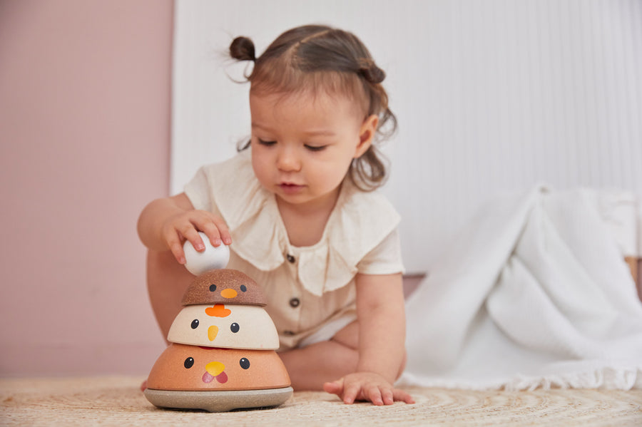 Young girl sat on the floor smiling and looking at her stack of PlanToys wooden nesting chicken bowls