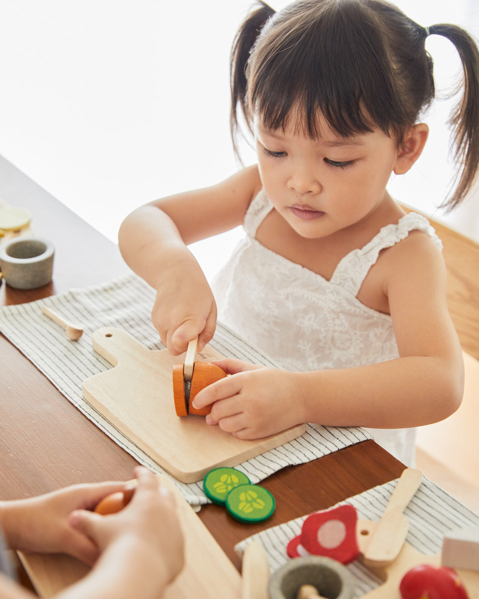 Young girl cutting pieces of play food with the wooden knife from the PlanToys charcuterie board set