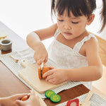 Young girl cutting pieces of play food with the wooden knife from the PlanToys charcuterie board set