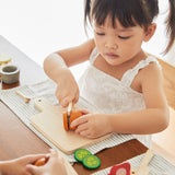 Young girl cutting pieces of play food with the wooden knife from the PlanToys charcuterie board set