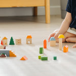 Close up of a childs hands playing with the PlanToys solid wood stacking countryside blocks on a white floor