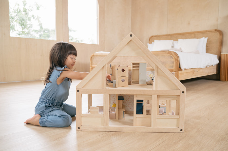 Young girl on her knees playing with the PlanToys eco-friendly dollhouse on a wooden bedroom floor