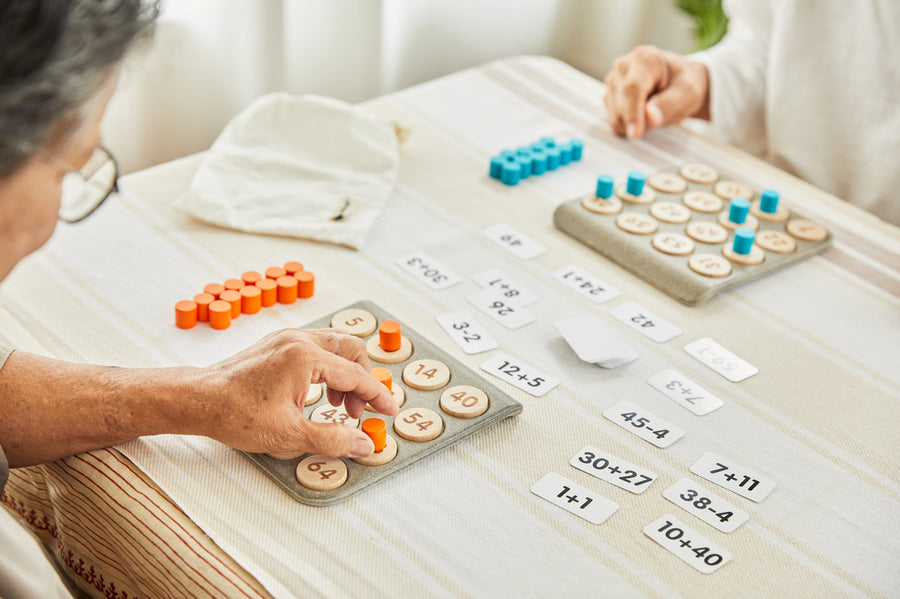 Close up of 2 people playing with the PlanToys wooden maths learning bingo game