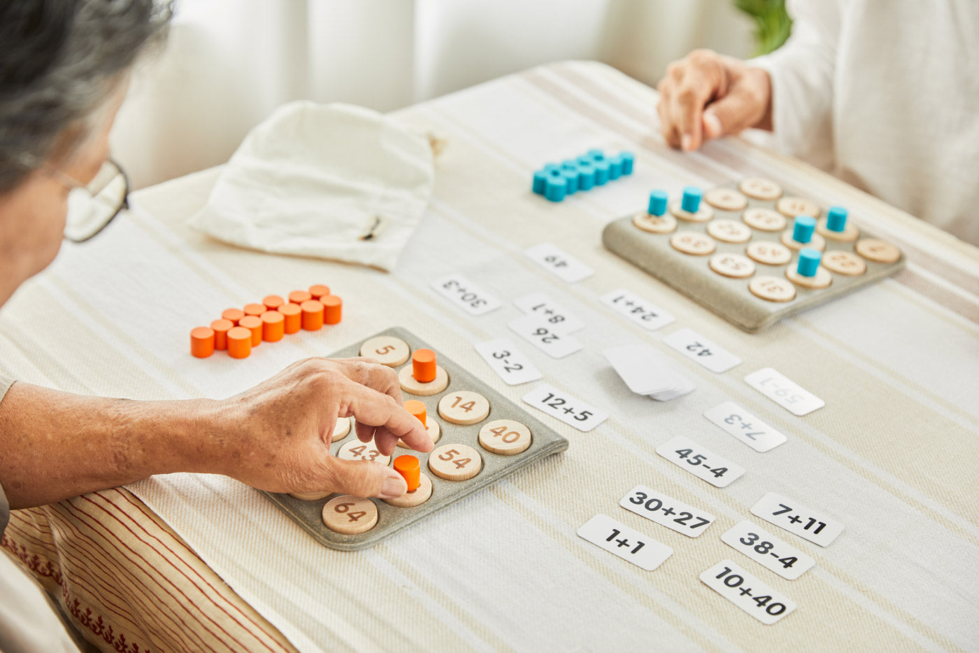 Close up of 2 people playing with the PlanToys wooden maths learning bingo game