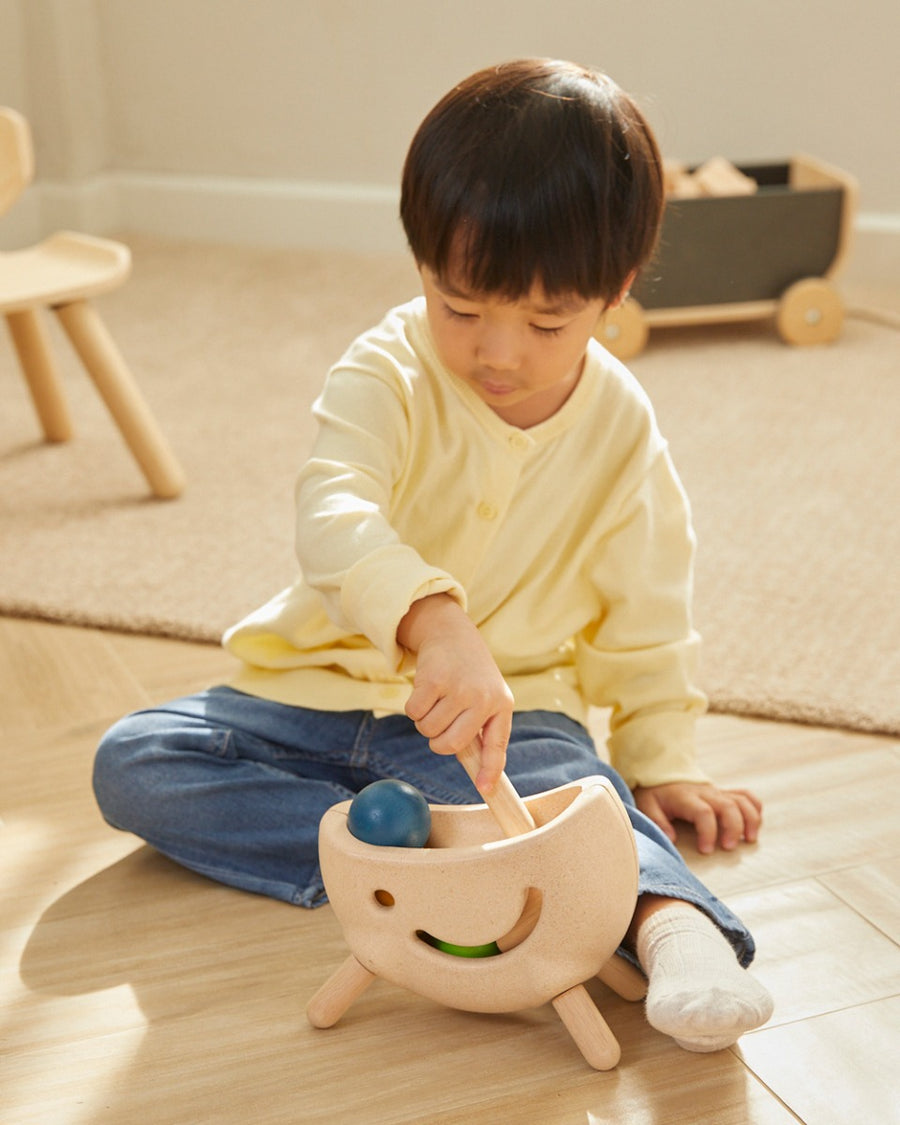 Young child sat on a wooden floor playing with the PlanToys miracle pounding toy