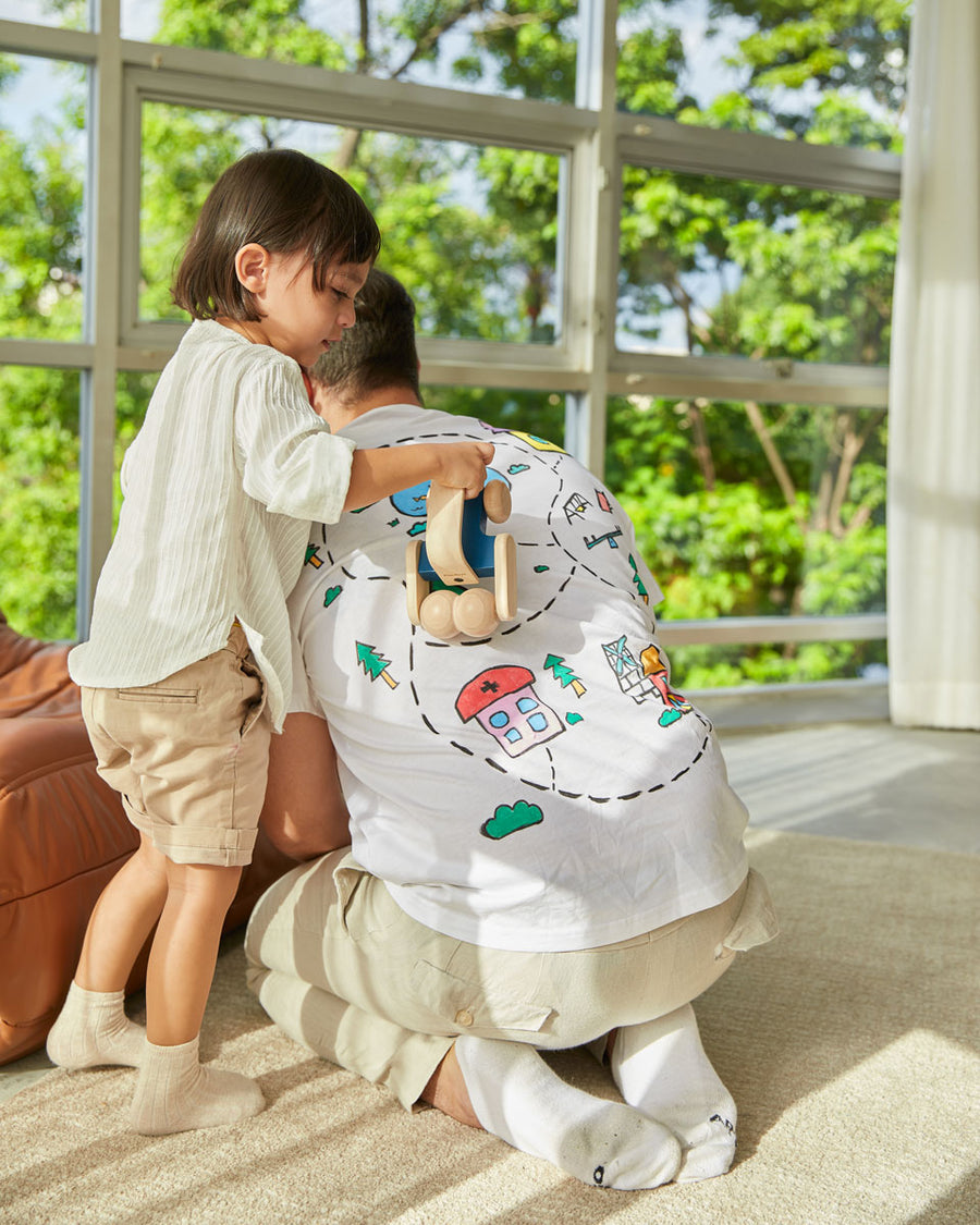 Man kneeling down with a child pushing the PlanToys wooden sensory roller vehicle toy across his back