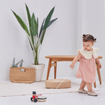 Girl pulling the PlanToys wooden musical drummer toy along a white floor next to a wooden table and potted plant