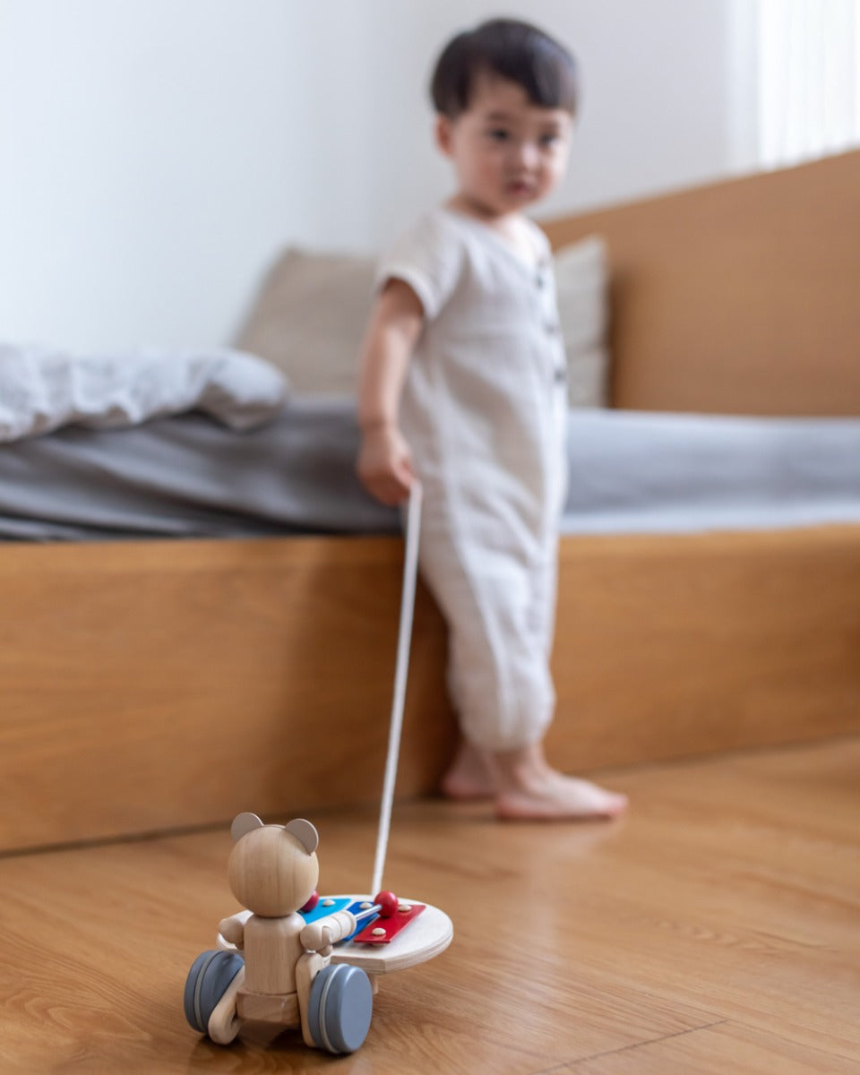 Close up of child pulling the PlanToys pull along musical bear toy on a wooden floor