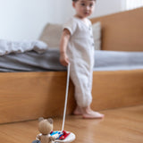 Close up of child pulling the PlanToys pull along musical bear toy on a wooden floor