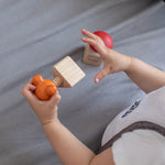 A child holding Orange Tap Bolt of the PlanToys Wooden Nuts and Bolts puzzle in a wooden Triangle block. The Plan Toys Red Button Bolt is below in a wooden square block.