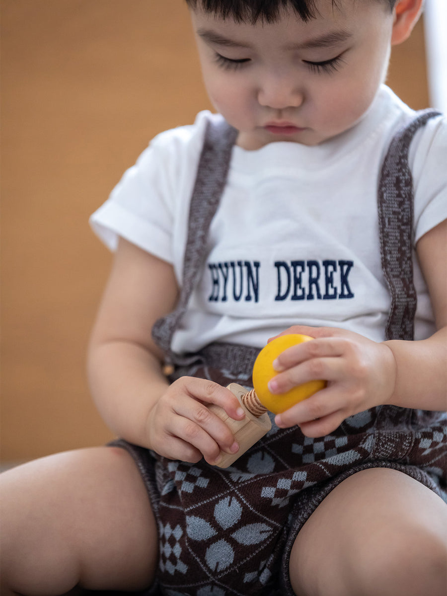 A child looking in concentration whilst putting in Yellow PlanToys Wooden Nuts and Bolts Puzzle Ball bolt into a wooden block.