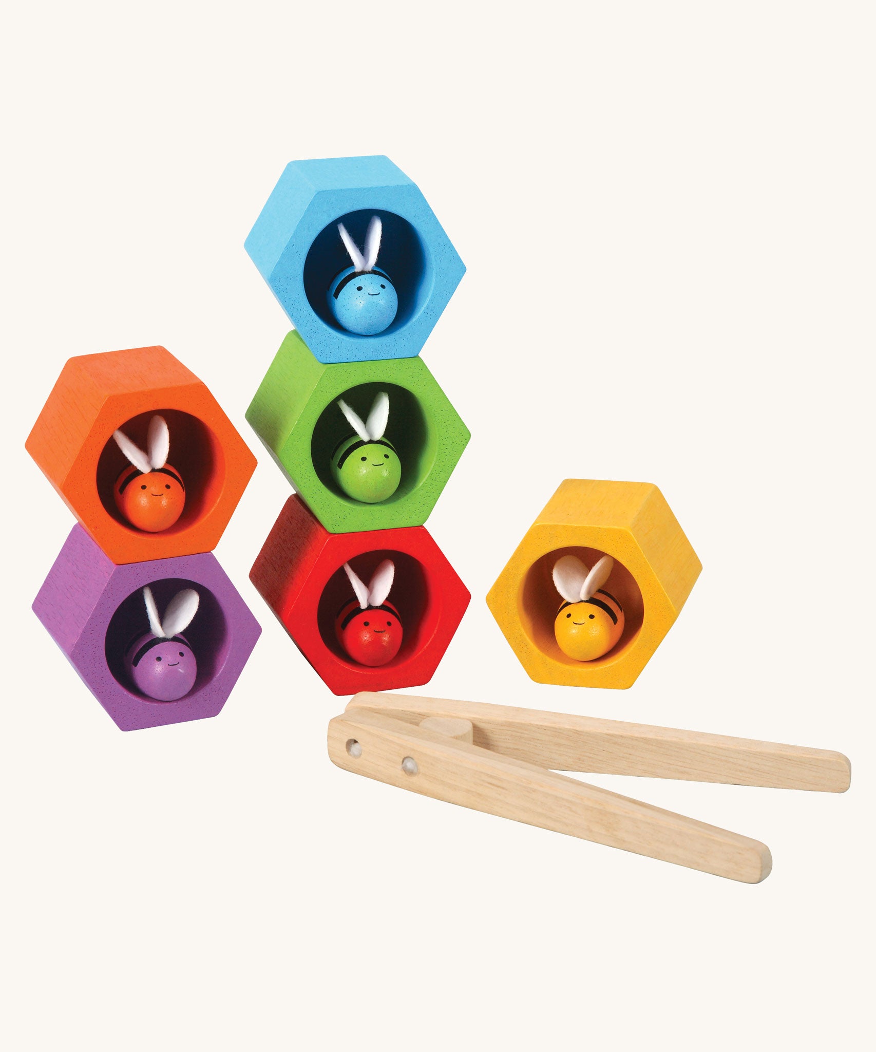 The PlanToys Bee Hives in the Rainbow colour way on a plain background. The bees are all in their matching coloured bee hive. The wooden tweezers can be seen placed in front of the hives. 
