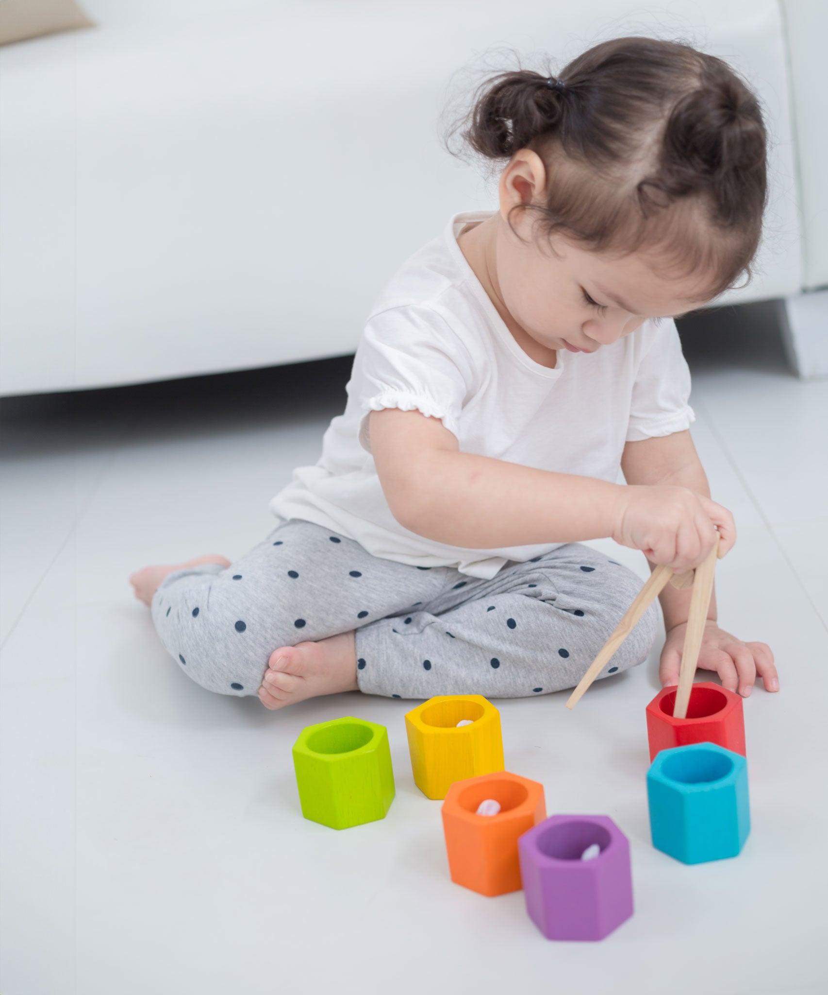 A child sitting on the floor in front of a sofa playing with the Plan Toys Bee Hives Rainbow set. 