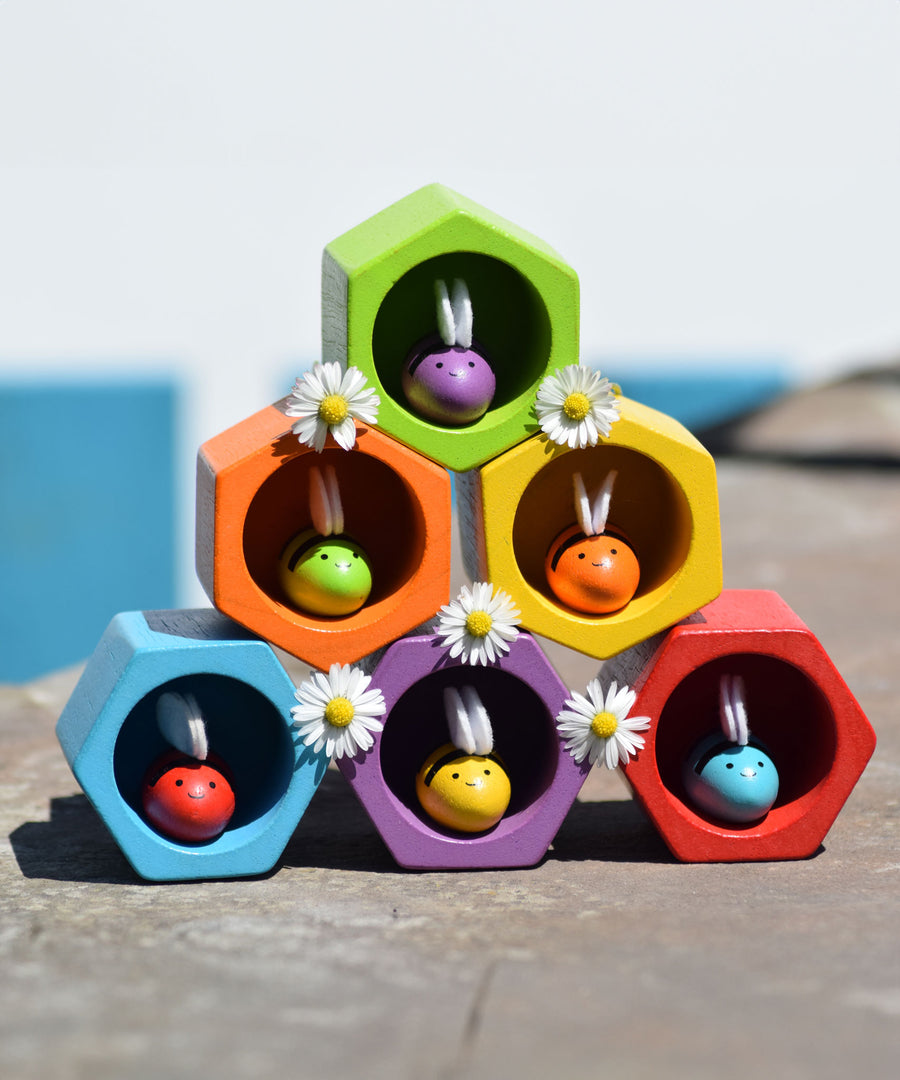 The PlanToys rainbow bee and bee hives set stacked up in a 3, 2, 1 formation. All the bees are in the hives daisies have been placed in-between the hives. 