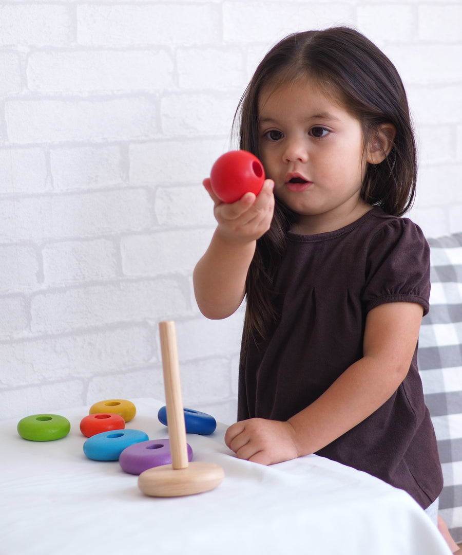 A child playing with the PlanToys Stacking Ring, the child is holding the red ball piece that sits on top of the rod.