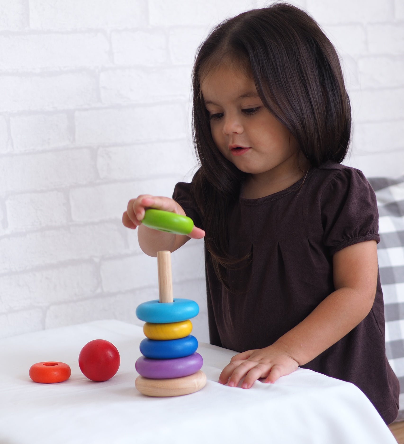 A child playing with the PlanToys Stacking Ring. The child is placing the green piece on the rodded base. 