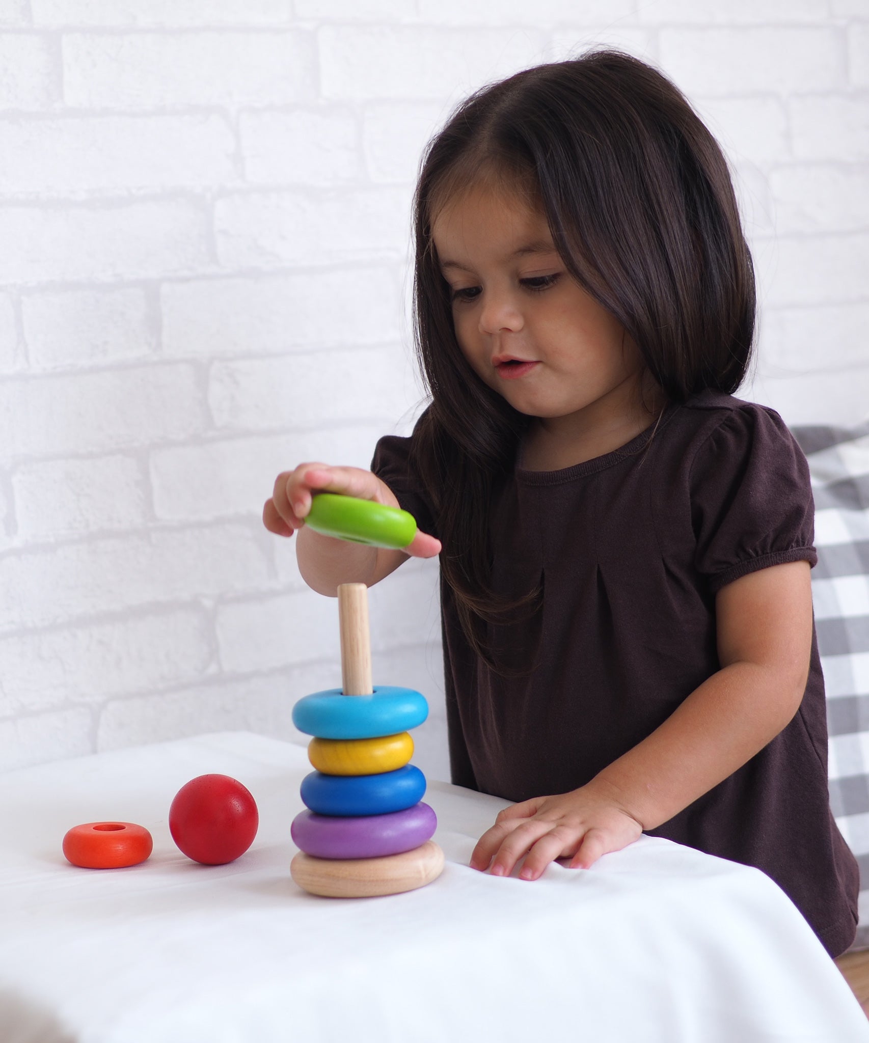 A child playing with the PlanToys Stacking Ring. The child is placing the green piece on the rodded base. 