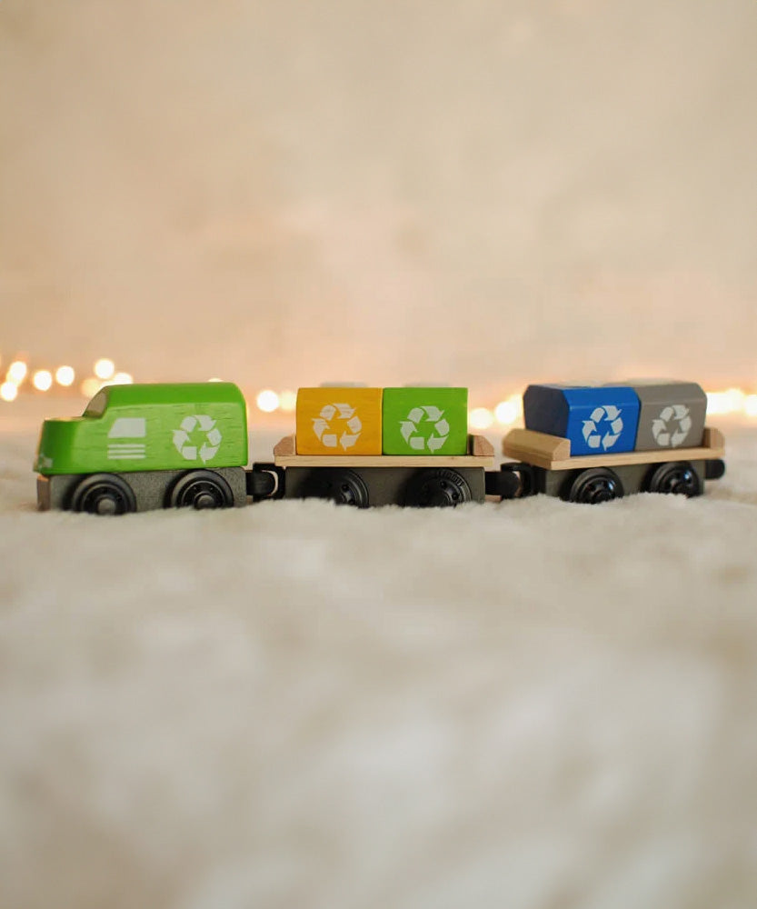 The PlanToys Recycling Train Toy placed on a fluffy surface in front of fairy lights.