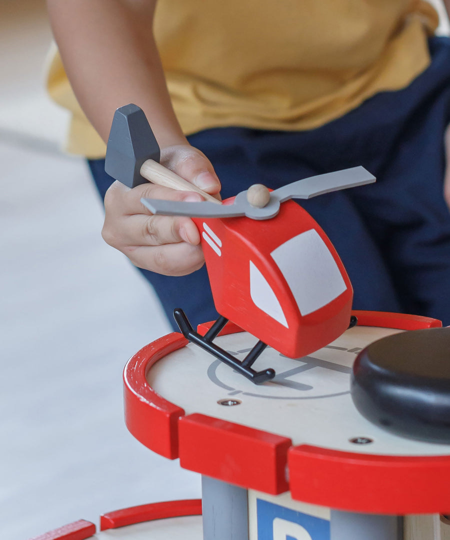 A close up of a child's hand playing with the PlanToys Helicopter on a PlanToys parking garage.