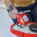 A close up of a child's hand playing with the PlanToys Helicopter on a PlanToys parking garage.