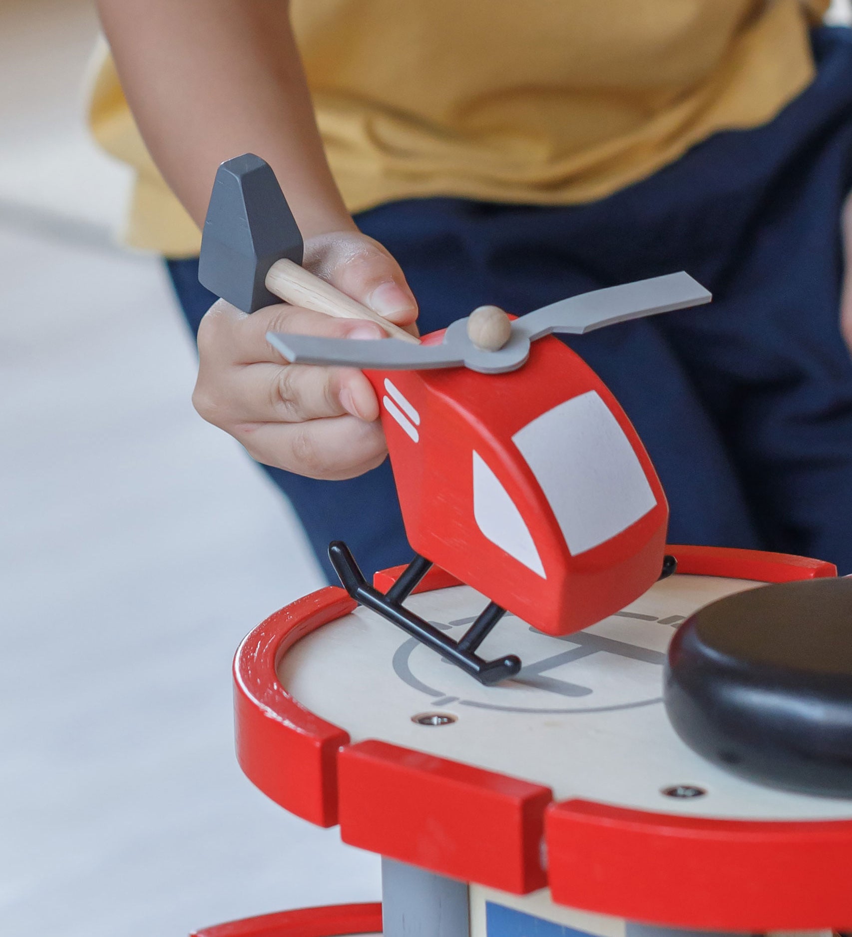 A close up of a child's hand playing with the PlanToys Helicopter on a PlanToys parking garage.