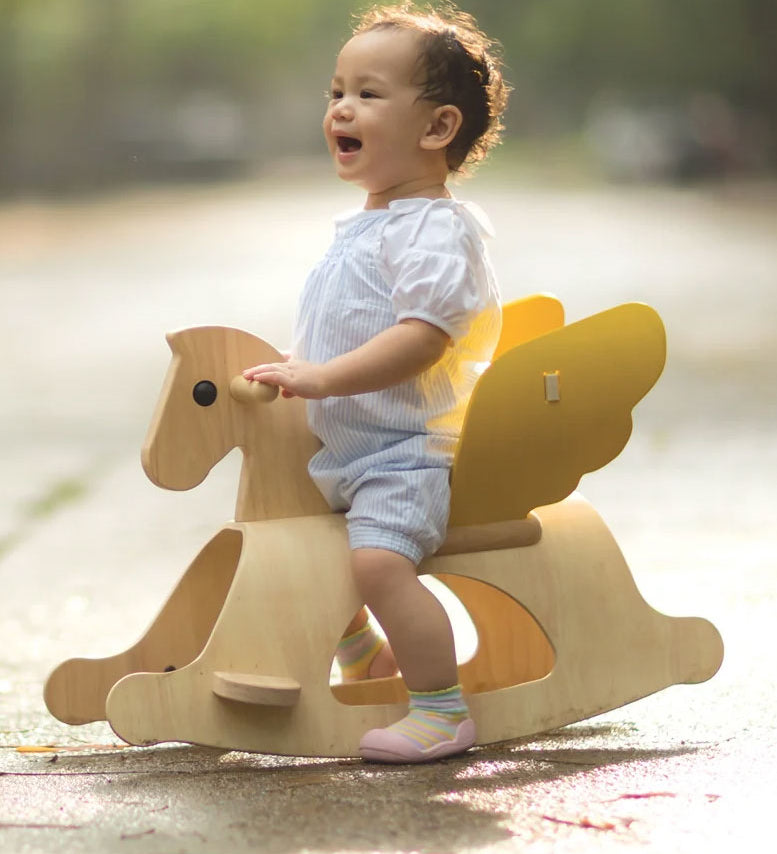 A child sitting on the PlanToys Rocking Pegasus toy. 