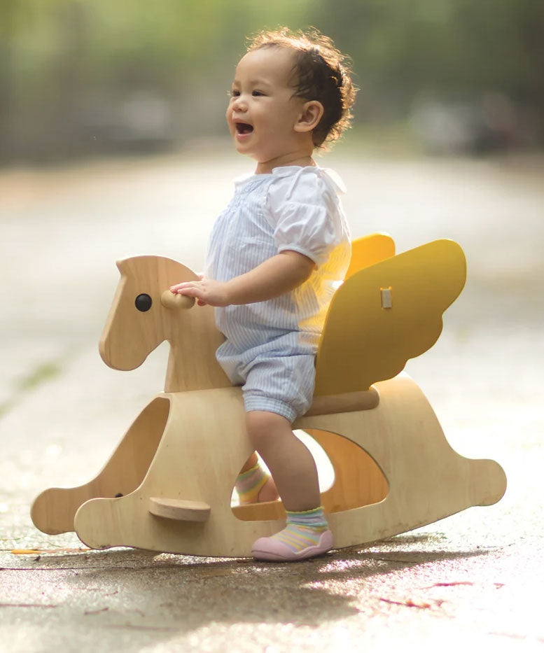 A child sitting on the PlanToys Rocking Pegasus toy. 