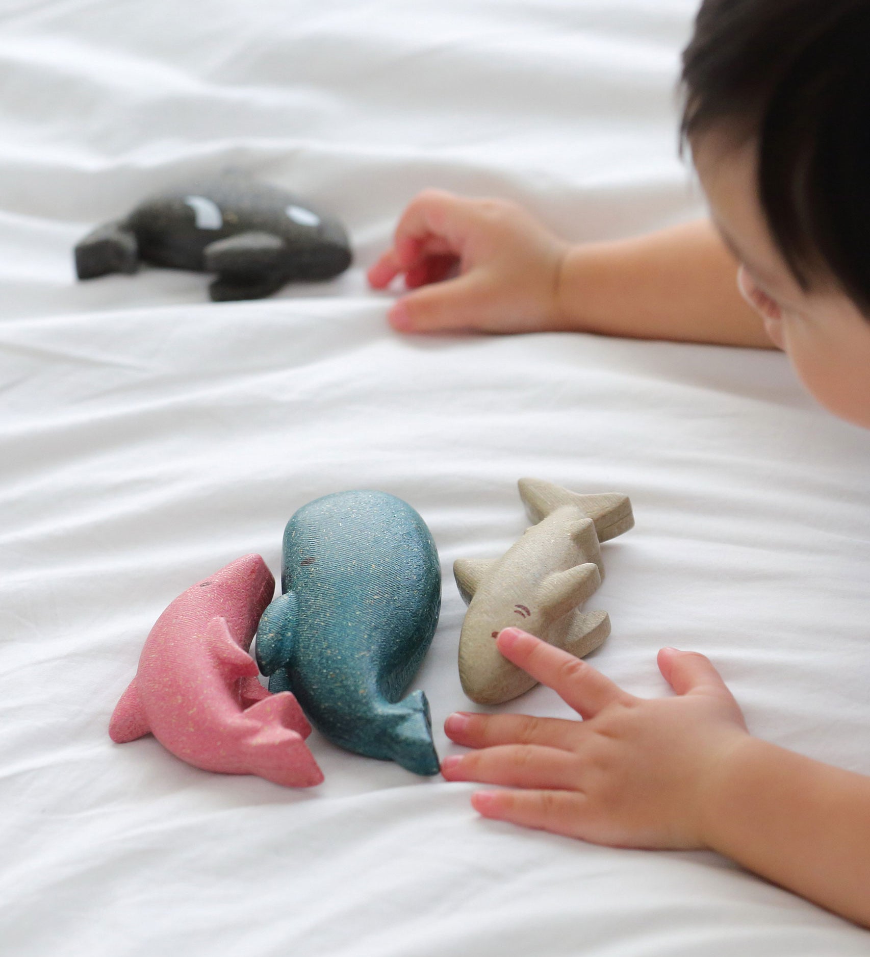 A close up of a child's hands playing with the figures from the PlanToys Sea Life Set. 