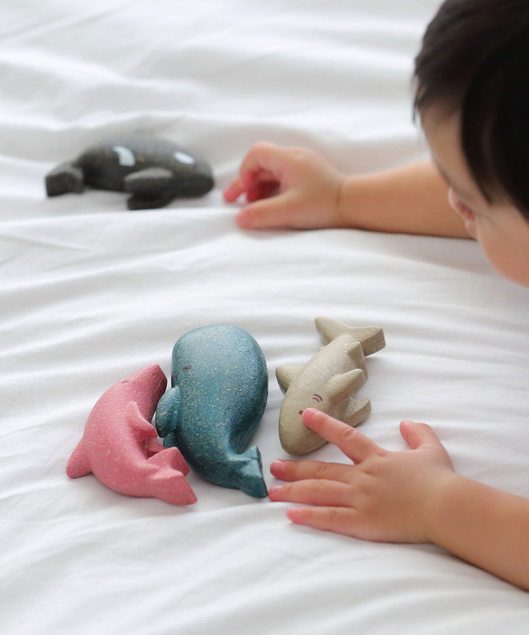 A close up of a child's hands playing with the figures from the PlanToys Sea Life Set. 