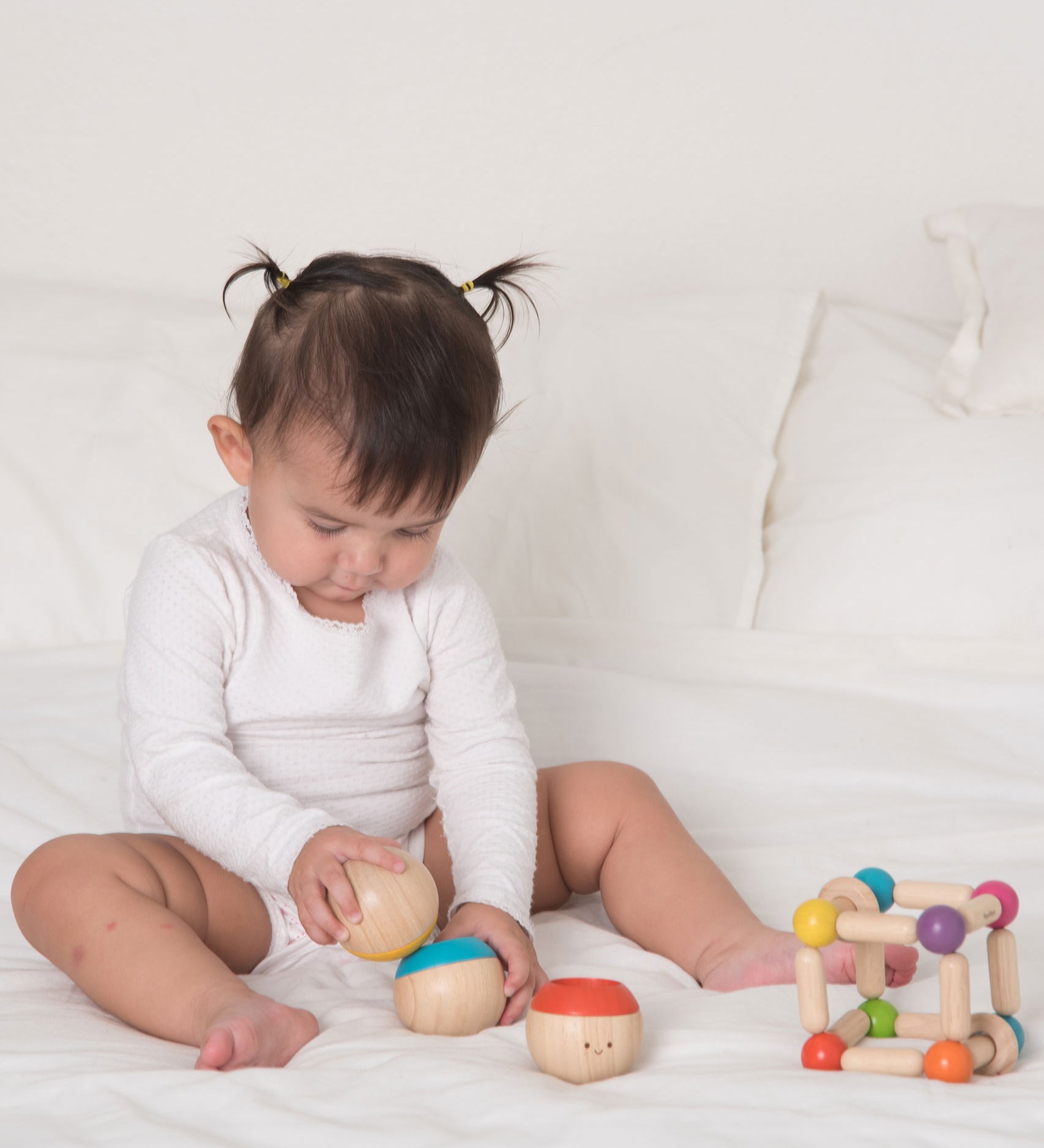 A baby playing with the Plan Toys Sensory Tumbling balls. The child is sitting on a bed. 