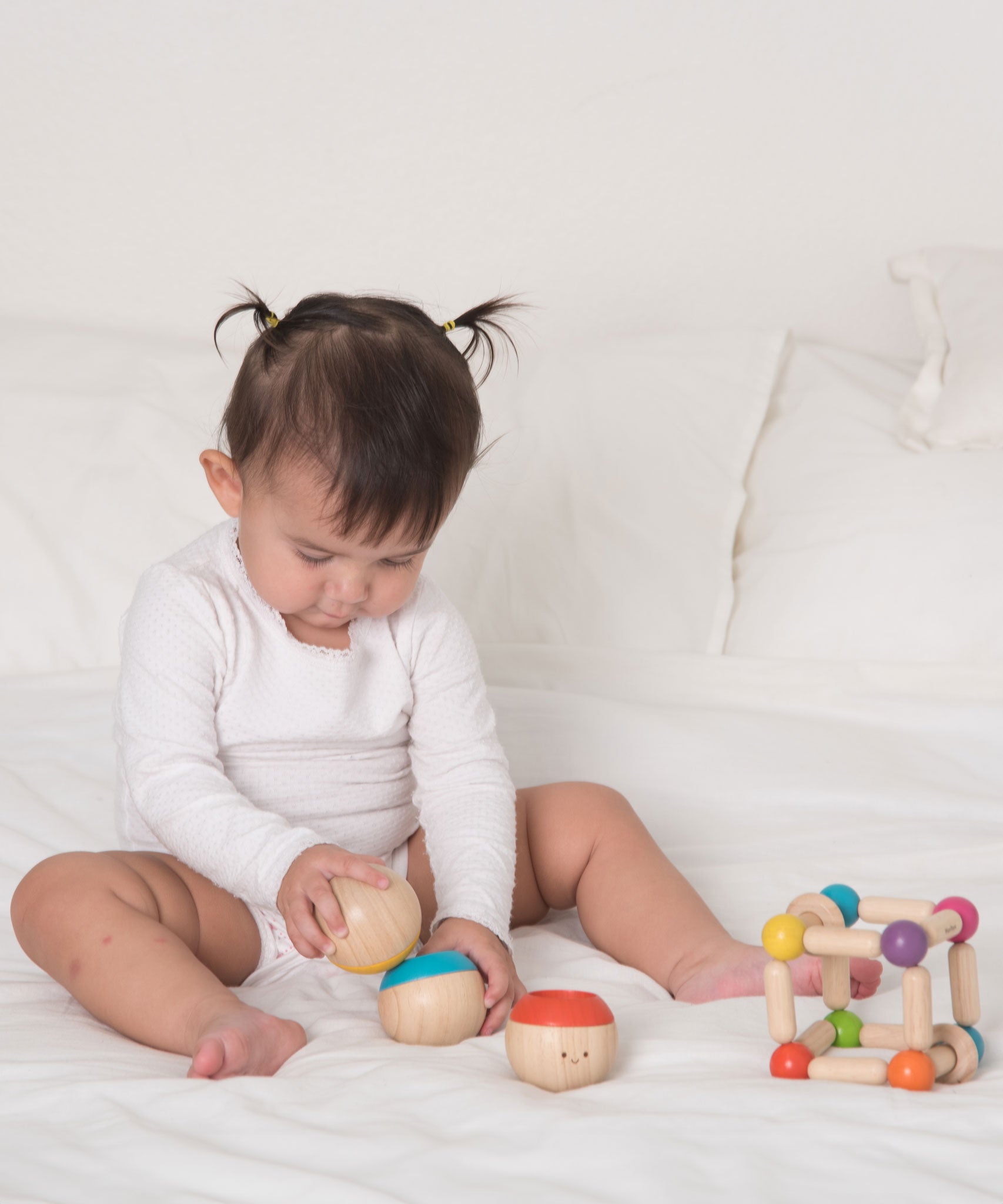 A baby playing with the Plan Toys Sensory Tumbling balls. The child is sitting on a bed. 